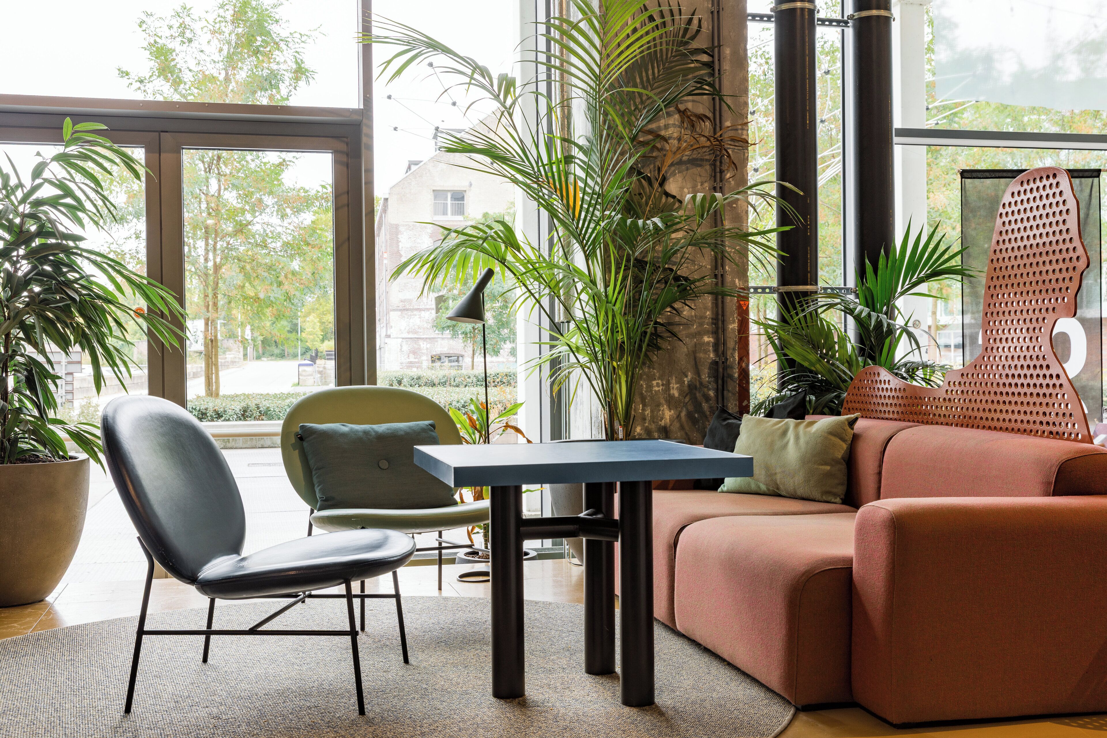 Un salon moderne comprenant un canapé, un fauteuil, une table et de grandes fenêtres donnant sur l’extérieur.