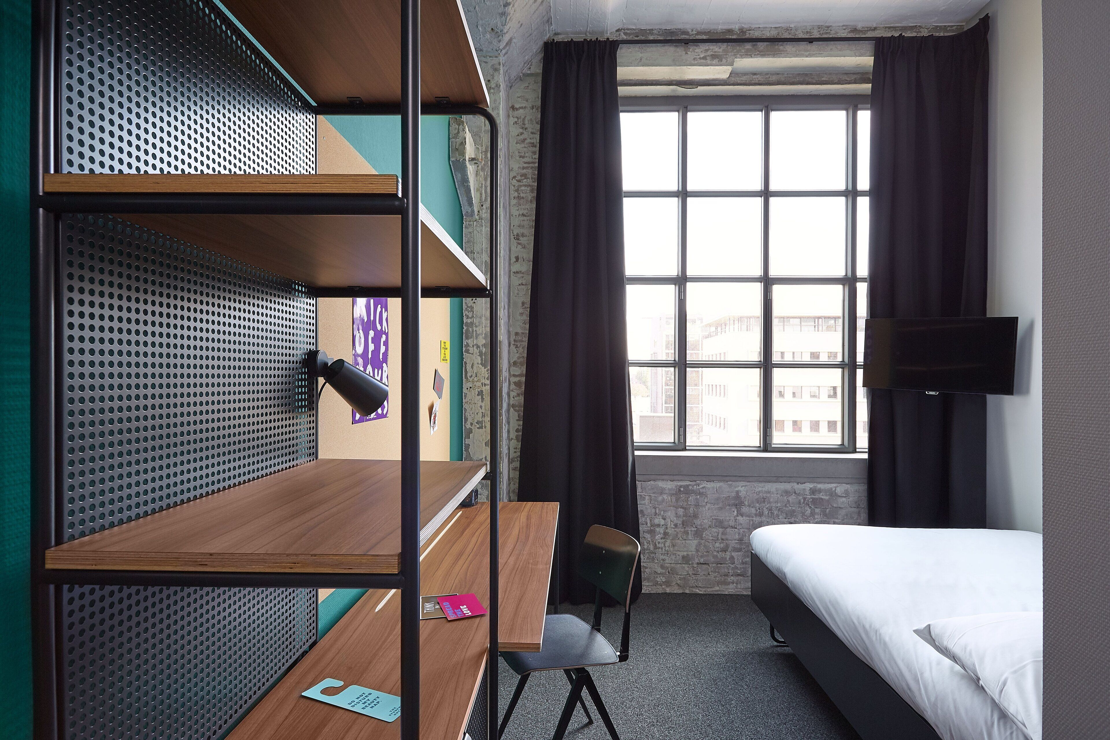 A dormitory room with bunk beds, a desk, a chair, a bed, a TV, and a window with curtains.