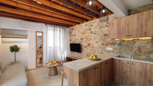 A modern kitchen with a stone wall, wooden cabinets, and a built-in TV. - Lindos Citrin Suites (Rhodes)