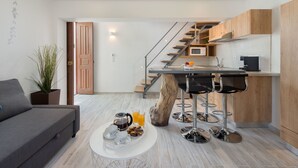 A modern kitchen with a central island, a dining area with a sofa and coffee table, and a staircase leading to an upper level. - Lindos Citrin Suites (Rhodes)