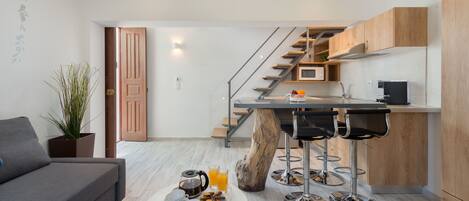 Eine moderne Küche mit Kochinsel, ein Essbereich inklusive Sofa und Couchtisch sowie eine Treppe, die in ein Obergeschoss führt.