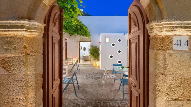 An entrance with a stone archway leading to a courtyard with a cobblestone floor, a small table, and chairs. - Lindos Citrin Suites (Rhodes)