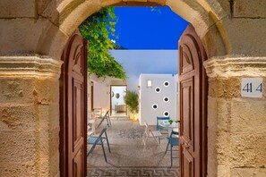 An entrance with a stone archway leading to a courtyard with a cobblestone floor, a small table, and chairs. - Lindos Citrin Suites (Rhodes)