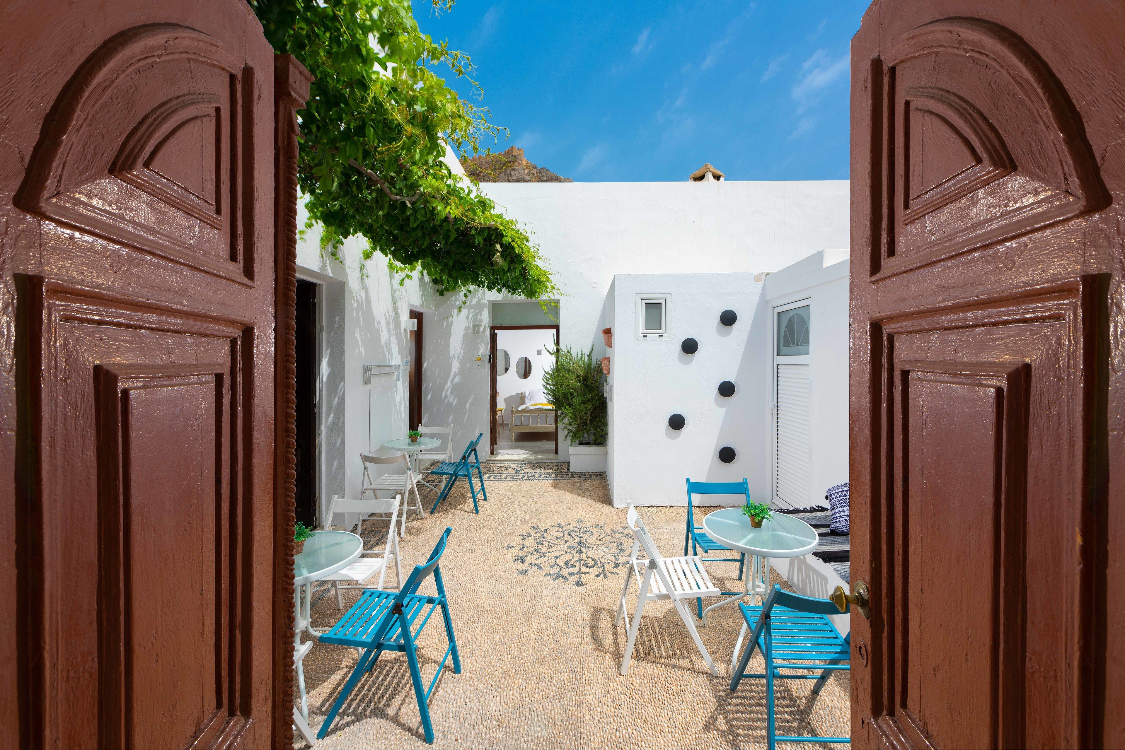 A courtyard with white walls, blue chairs, and a small table.