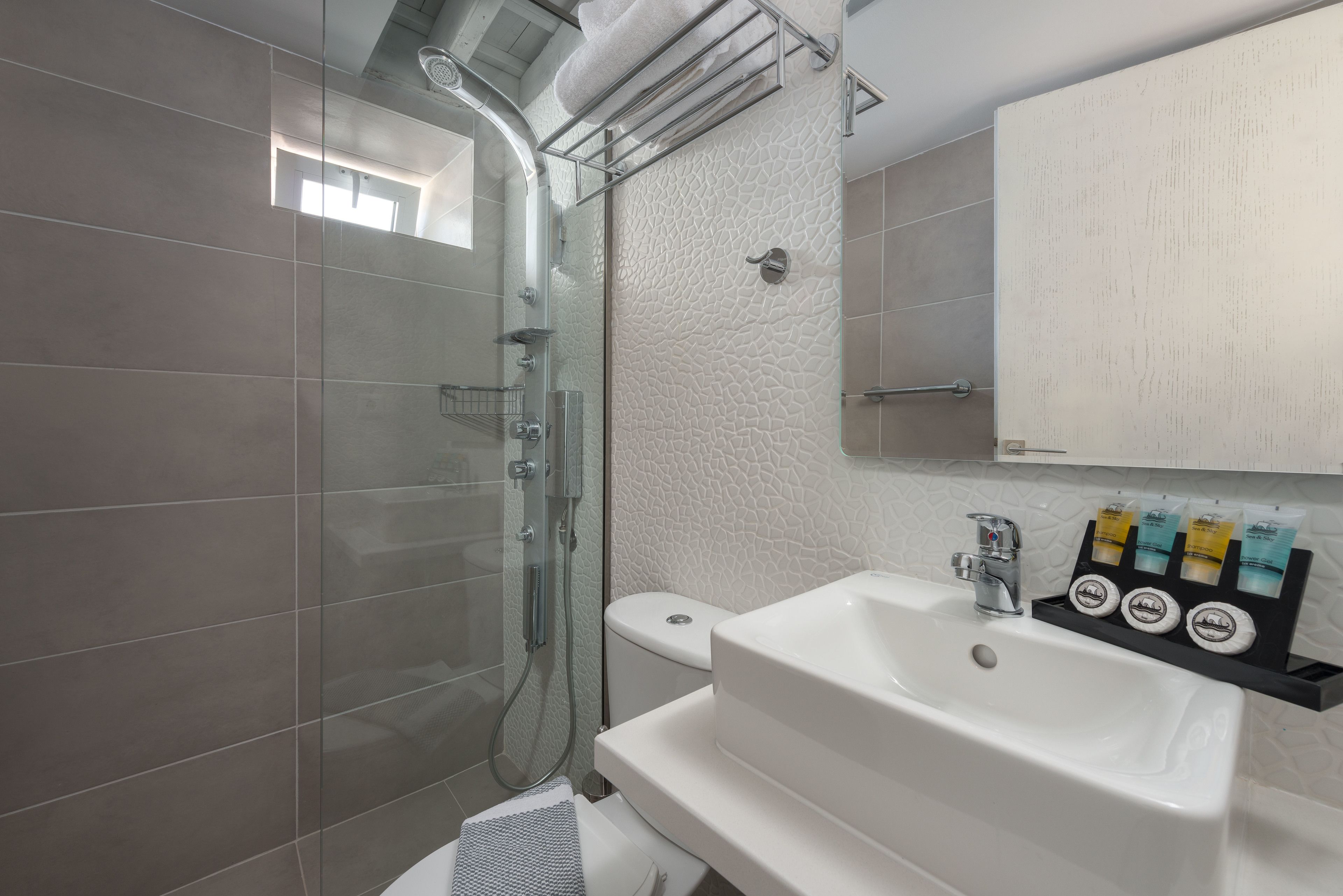 A modern bathroom with a glass-enclosed shower, a white sink with soap dispensers, and a towel rack.