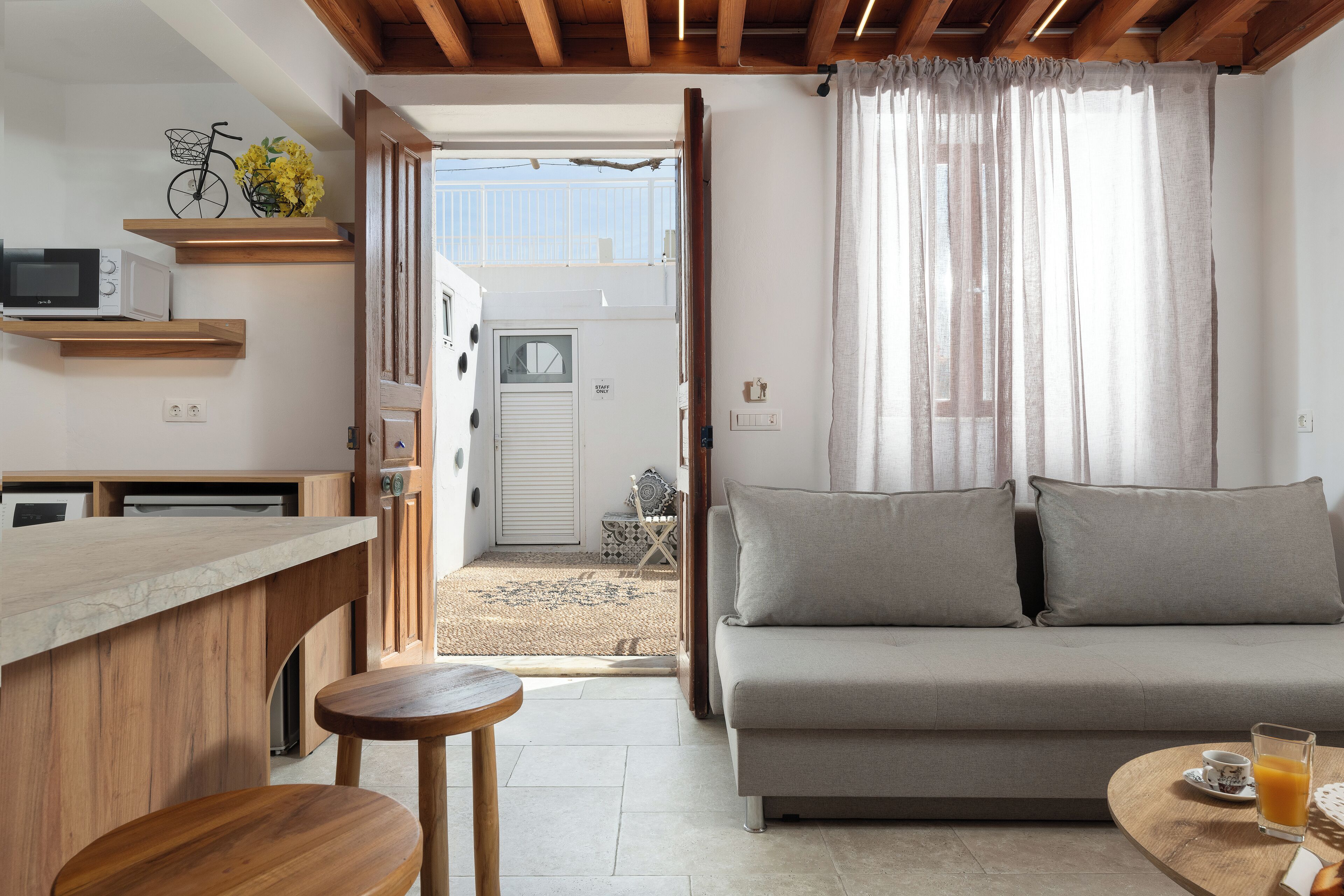 A modern kitchen with wooden shelves, a microwave, and a dining area with a sofa and a table.