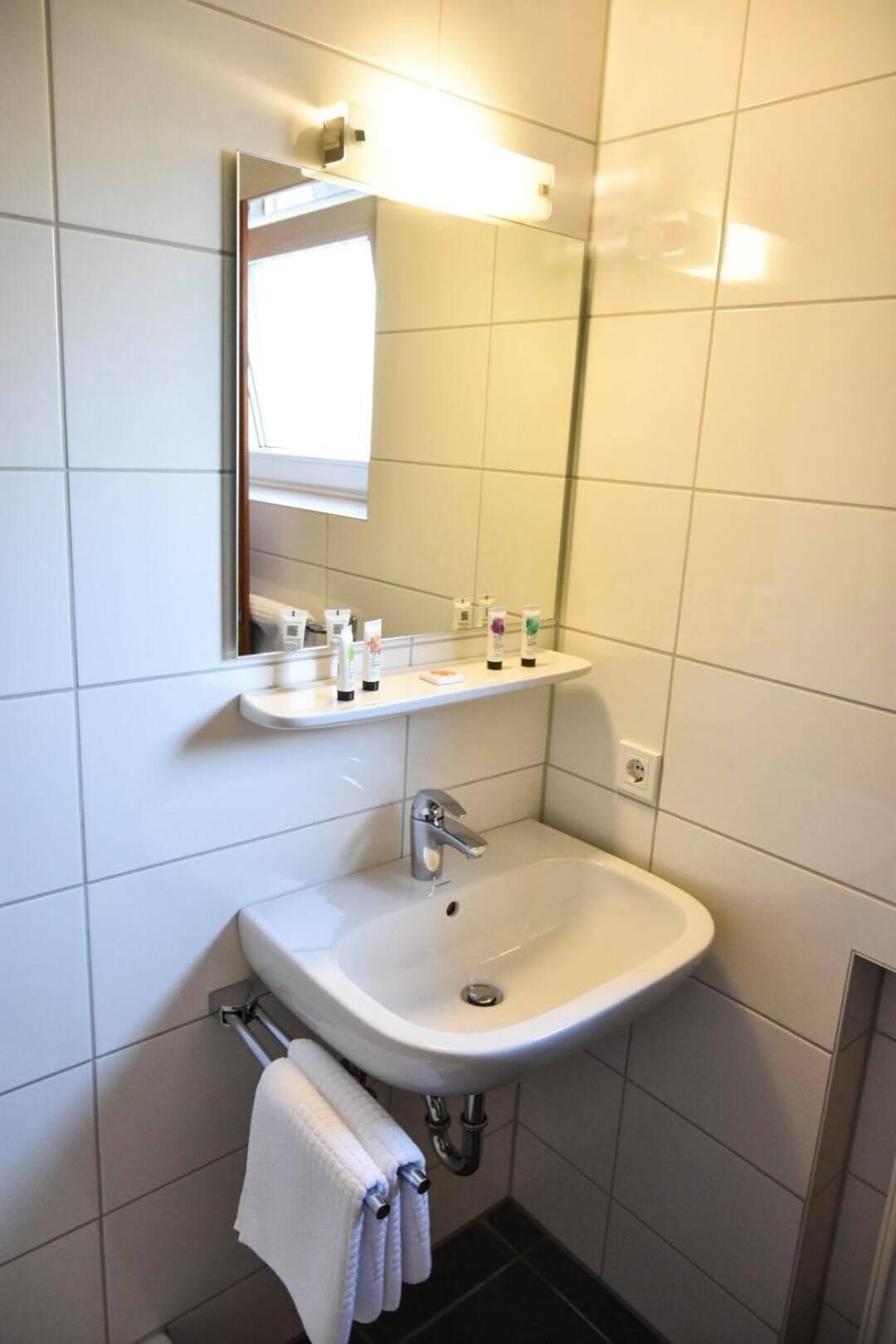 A bathroom with a white sink, a mirror, and a shelf with toiletries.