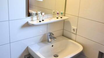 A bathroom with a white sink, a mirror, and a shelf with toiletries.