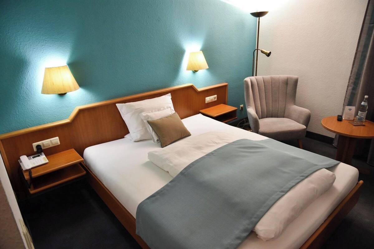 A hotel room with a bed, two bedside lamps, a chair, a small table, and a phone on the nightstand.
