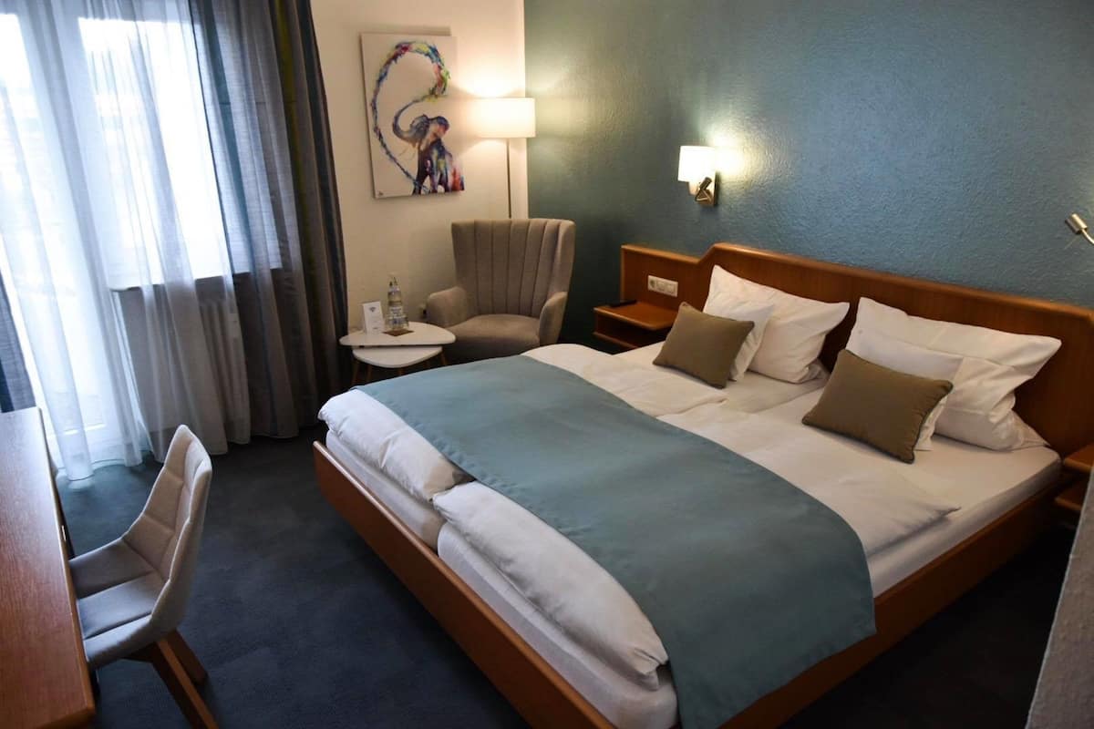 A hotel room with a large bed, a chair, a small table, and a lamp.
