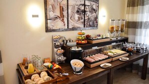 A buffet setup with various food items, including fruits, pastries, and meats, arranged on a wooden table with a modern abstract painting above.