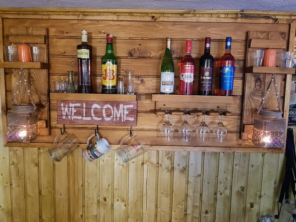 A wooden bar area with a 'WELCOME' sign, various bottles of alcohol, and glasses.