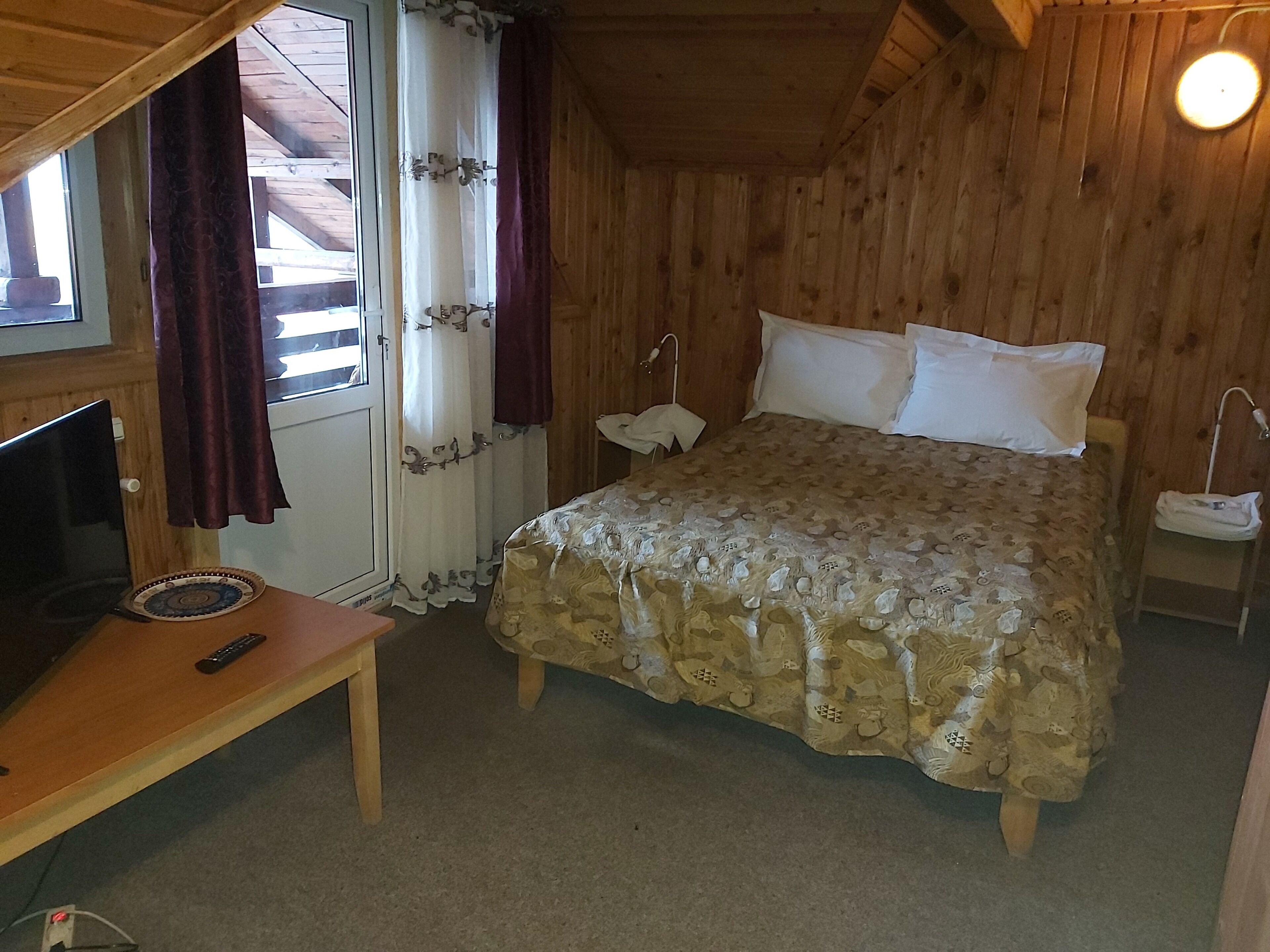 Una habitación de madera con cama, escritorio, televisor y cortinas.