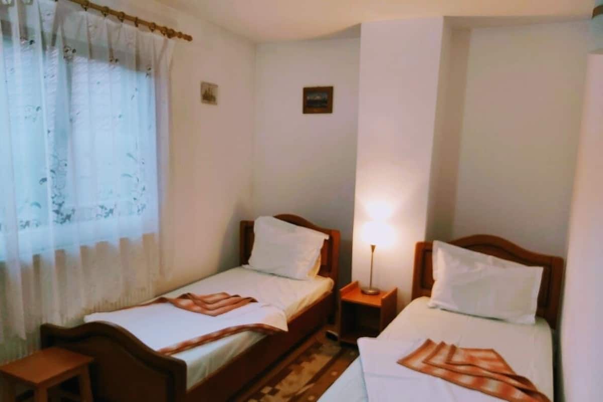 A room with two single beds, wooden headboards, a small bedside table, a nightstand, and a lamp.