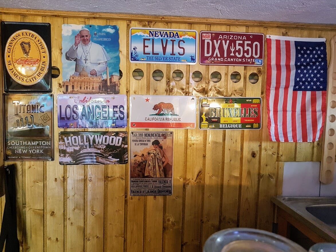 A wall with various travel-themed signs, including Nevada Elvis, Los Angeles, Hollywood, and a Belgian sign.