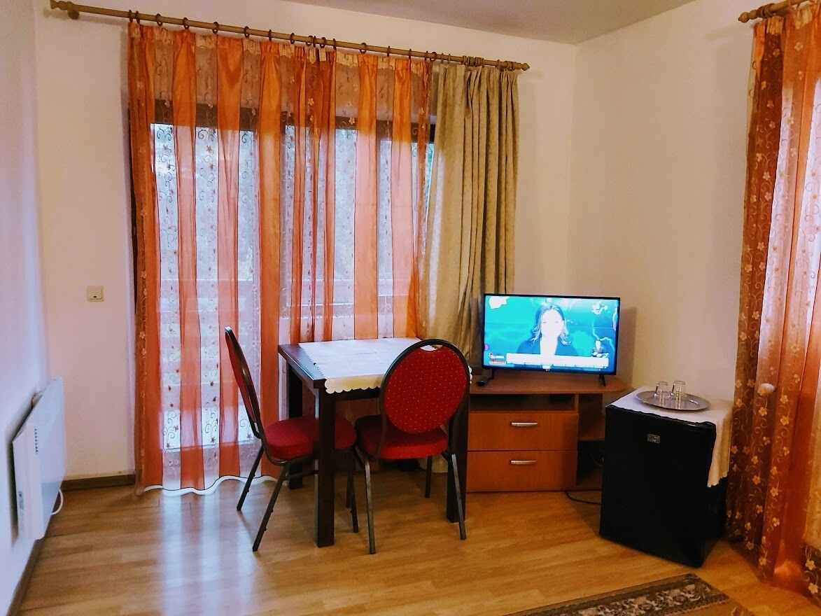 Een kleine kamer met een houten bureau, twee rode stoelen, een televisie en een kleine zwarte speaker.