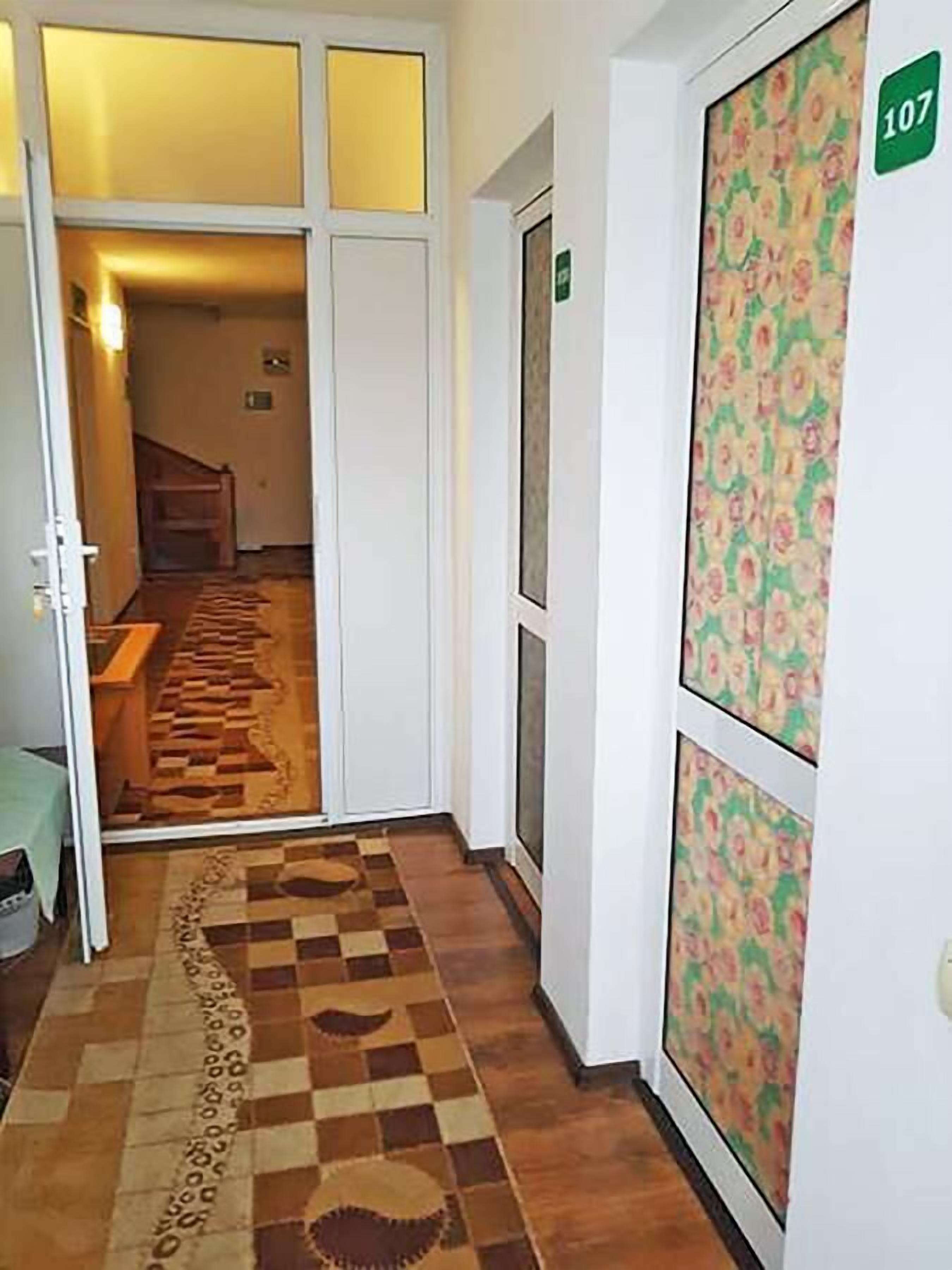 Um corredor com carpete xadrez, uma porta com padrão floral e uma placa indicando o quarto 107.