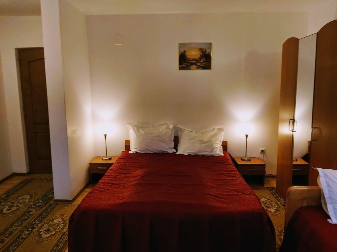 A hotel room with a large bed, two bedside tables, a nightstand, a lamp, a painting on the wall, and a wooden wardrobe.