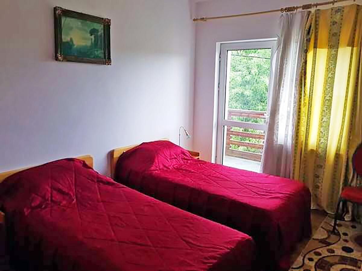 A room with two single beds, a window with curtains, a painting on the wall, and a chair near the window.