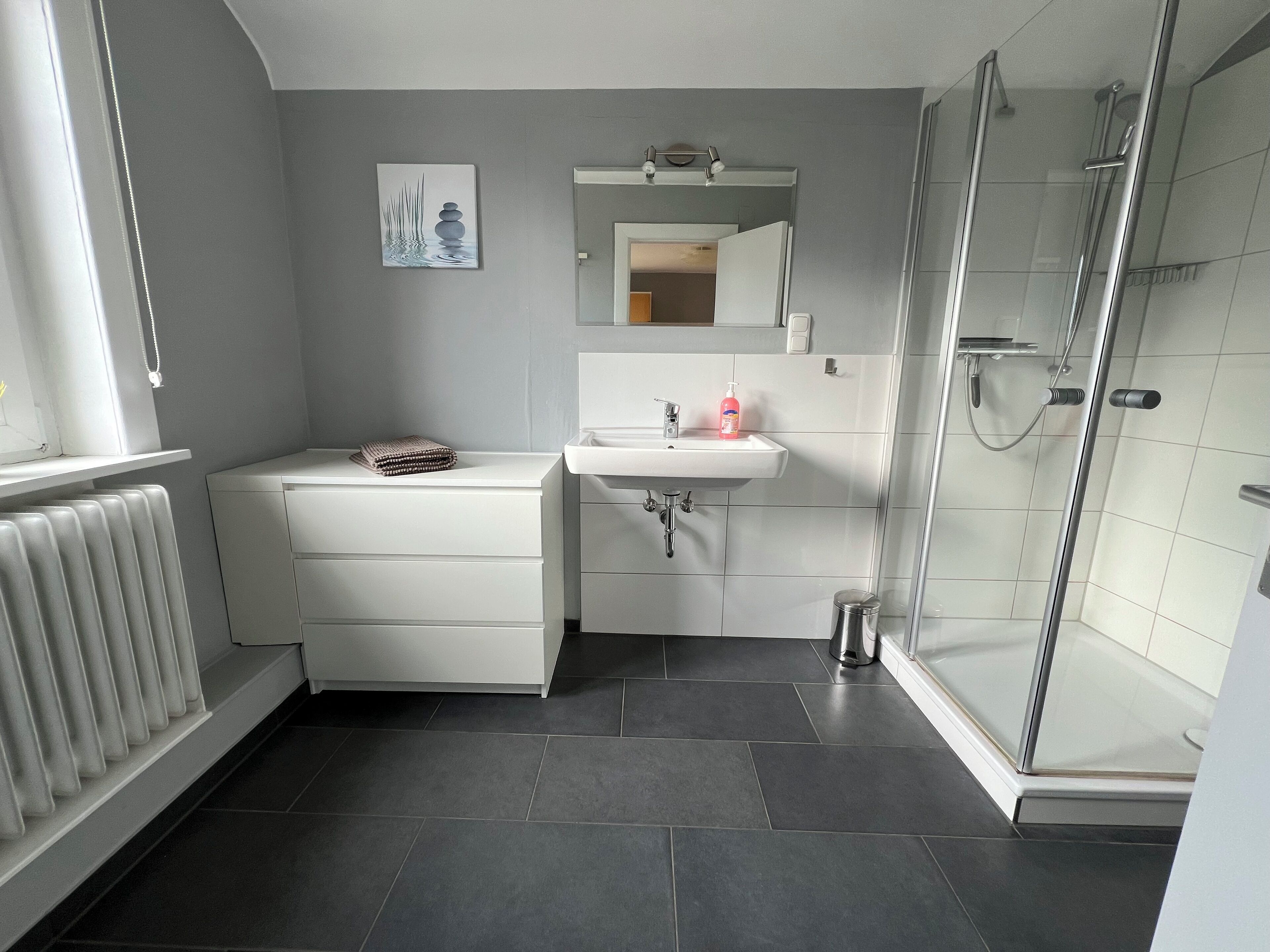 A modern bathroom with a white vanity, a sink with a mirror, and a glass shower enclosure.