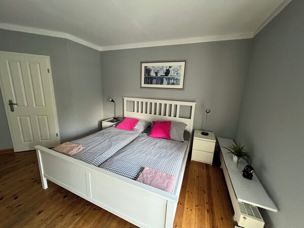 A bedroom with a white bed, two bedside tables, a nightstand, a framed picture on the wall, and a door.