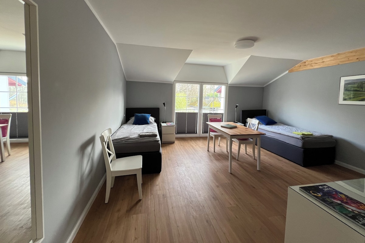 Un dormitorio moderno y compacto con techo inclinado, una cama, un escritorio y una silla.