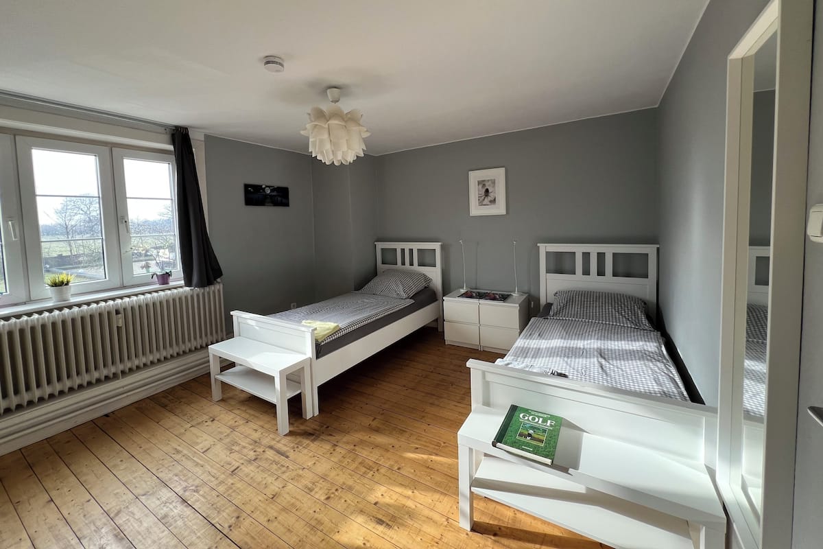 Un dormitorio con dos camas individuales, un radiador, una ventana con cortinas y un ventilador de techo.