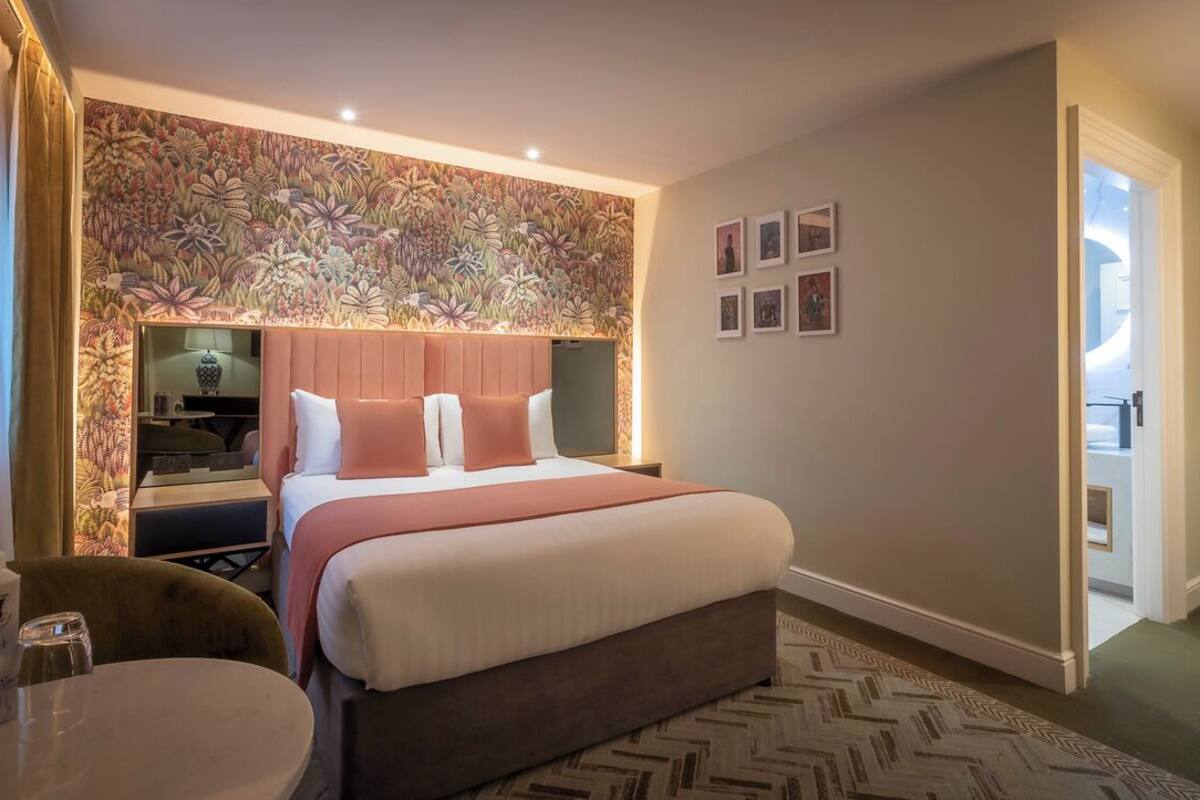 A hotel room with a large bed, a bedside table with a lamp, a chair, and a small round table.