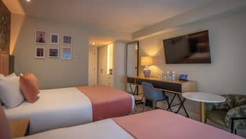 A hotel room with two beds, a desk with a computer, a TV, and a small round table.