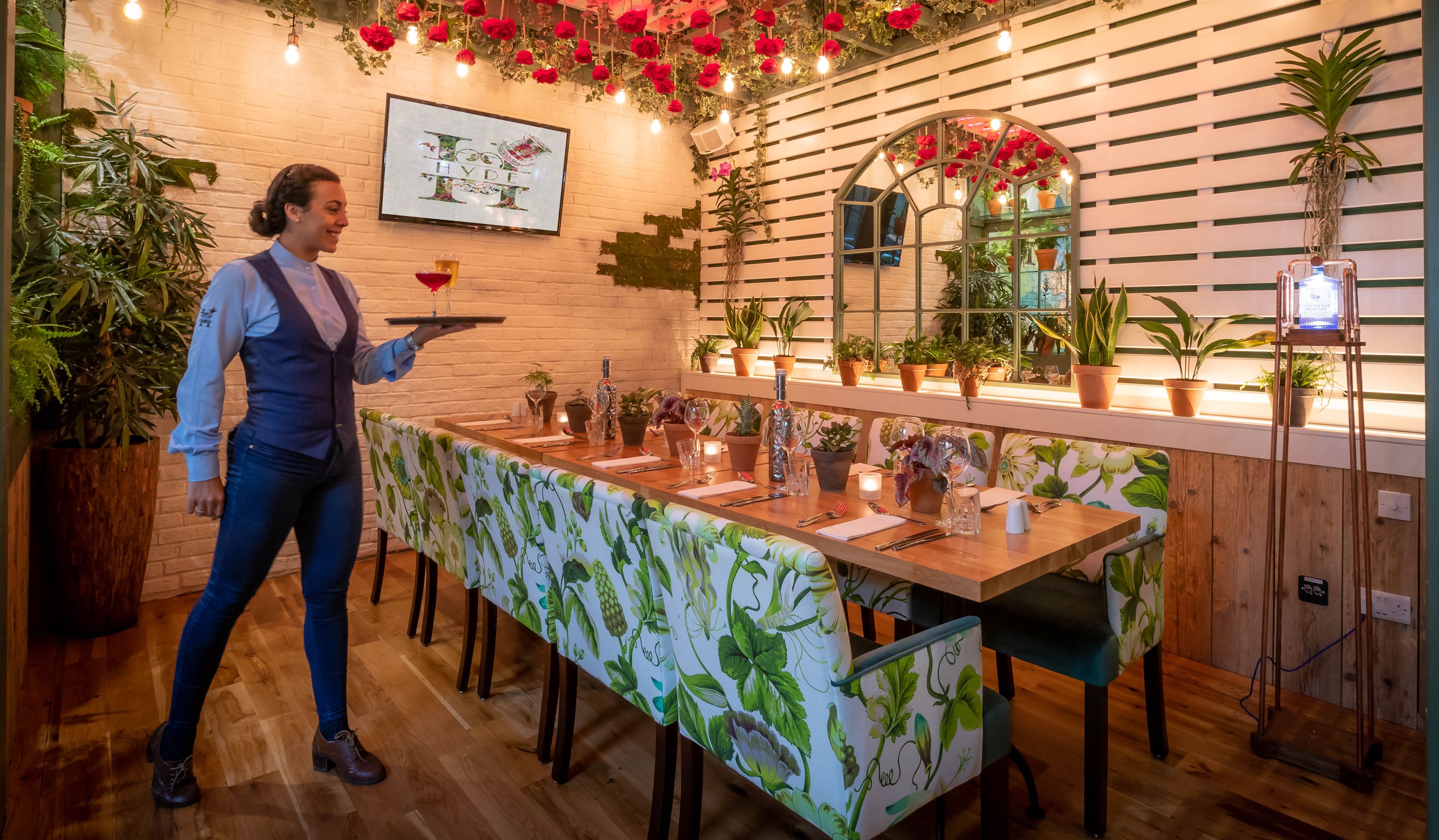 A restaurant interior with a long wooden table, potted plants, and a wall-mounted mirror.