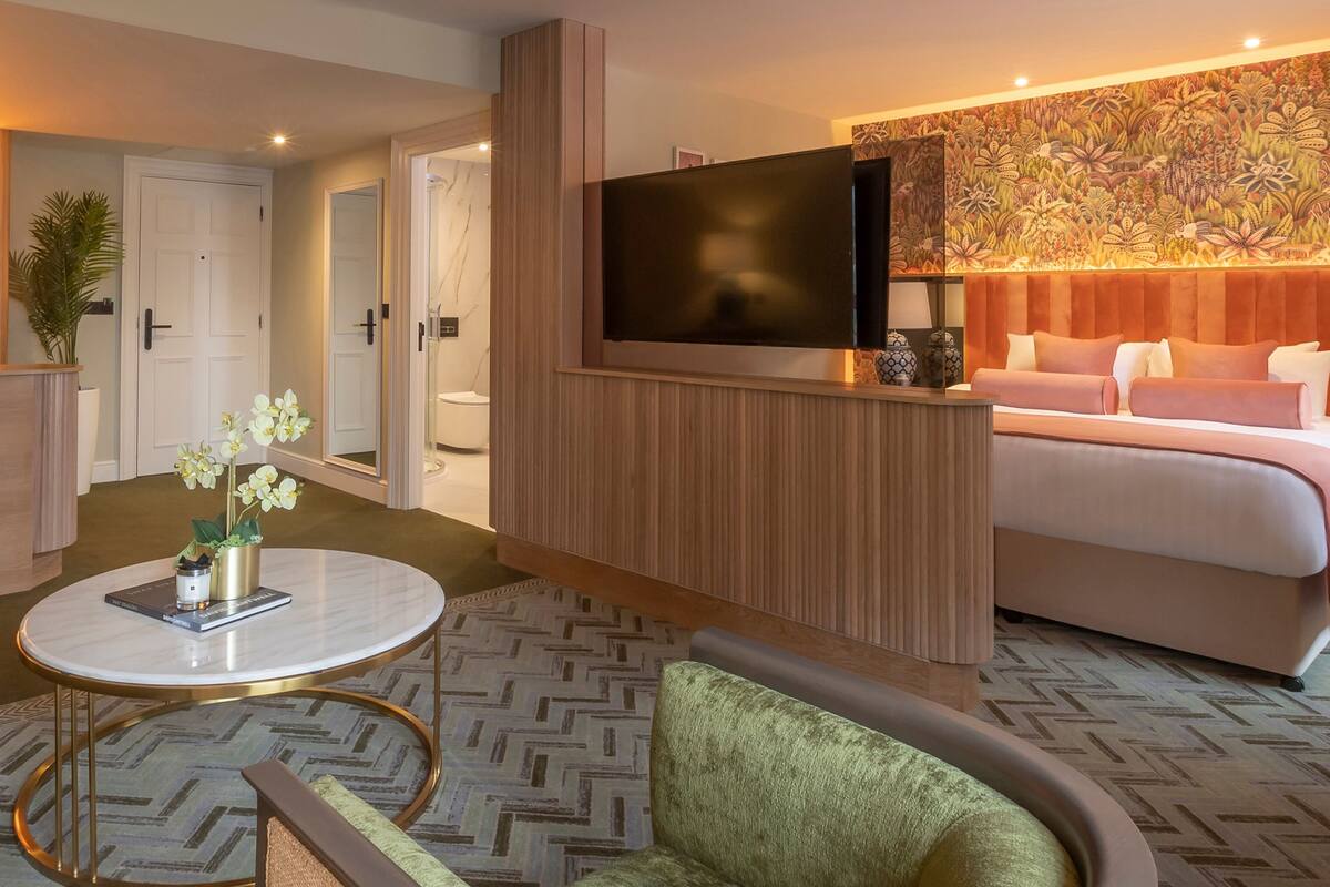 A hotel room with a TV, a sofa, a round table, and a small bar area.