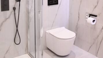 Un baño moderno con cabina de ducha de vidrio, inodoro blanco y pared de mármol.