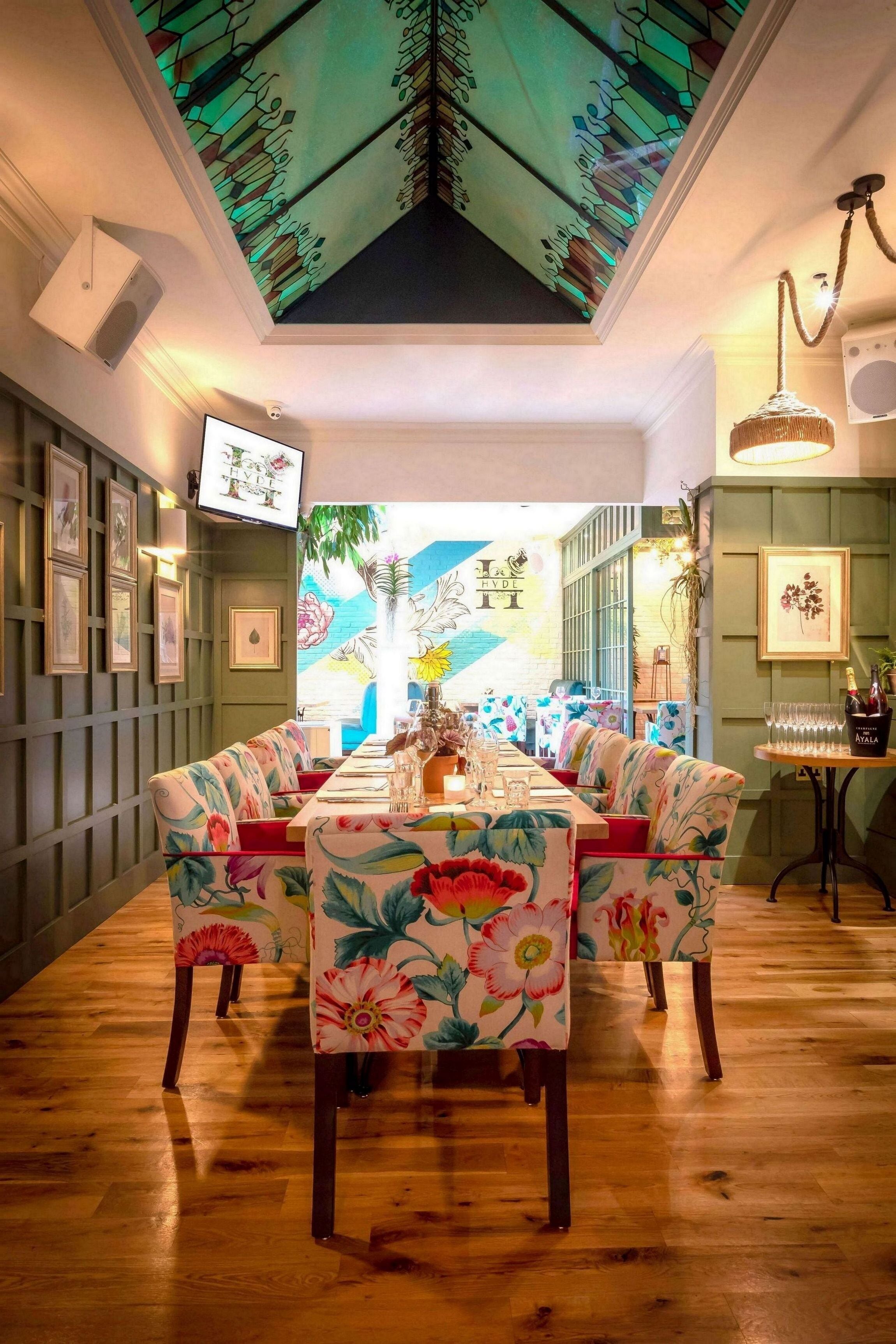 A dining area with a long table, floral-patterned chairs, and a ceiling with a stained glass design.