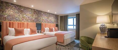 A hotel room with two beds, a desk, a chair, a patterned wall, and a window with curtains.