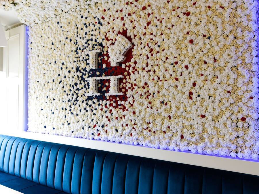 Pared decorada con flores blancas y rojas, un banco tapizado en azul y un diseño de pared estampado.
