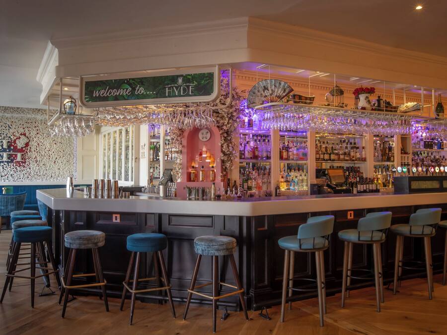 A bar area with a sign reading 'welcome to HYDE,' bar stools, a variety of bottles, and a decorative fan.