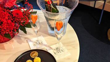 Una mesa con una botella de champán, dos copas, un plato de postre y un arreglo floral.