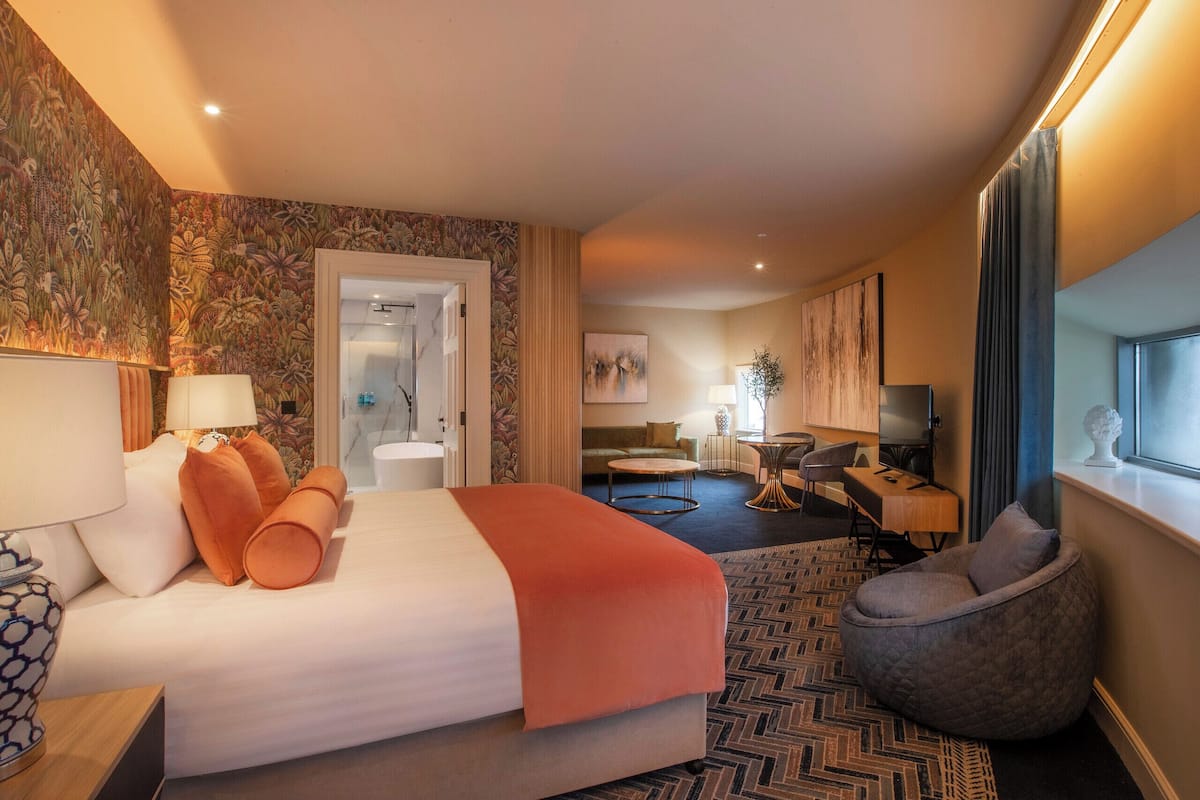 A hotel room with a large bed, a desk, a chair, and a seating area.