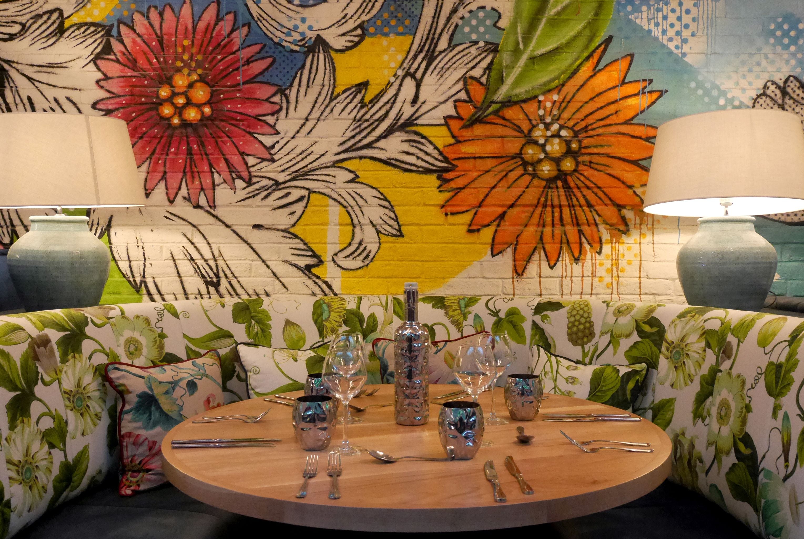 Una mesa redonda para comer con cristalería y cubiertos, rodeada por un sofá estampado con motivos florales.