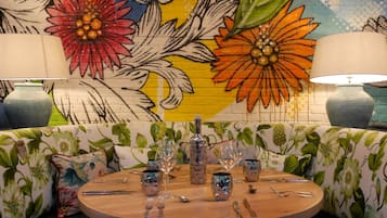 Una mesa redonda para comer con cristalería y cubiertos, rodeada por un sofá estampado con motivos florales.