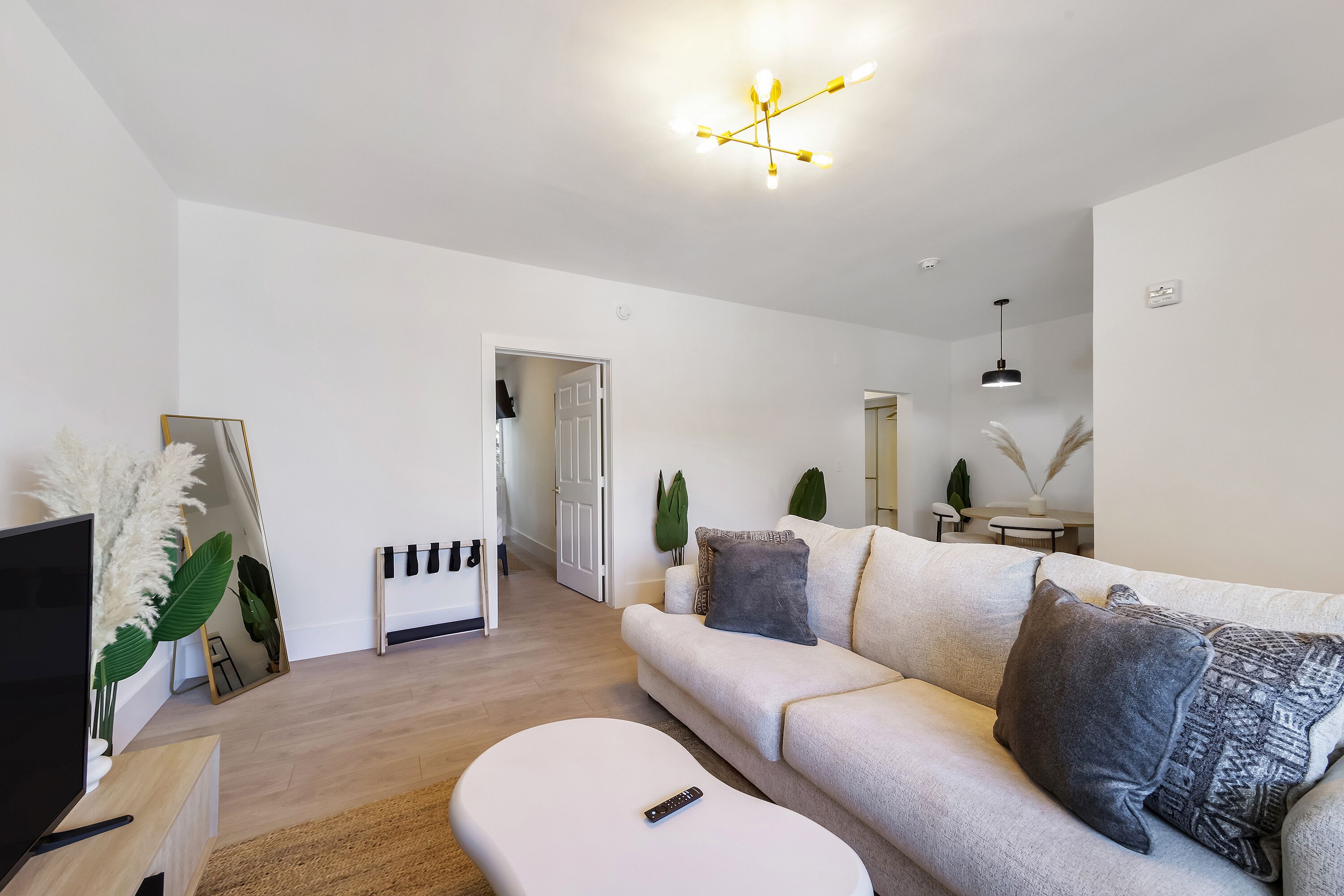 A modern living room with a sofa, a TV, a remote, and a ceiling light fixture.
