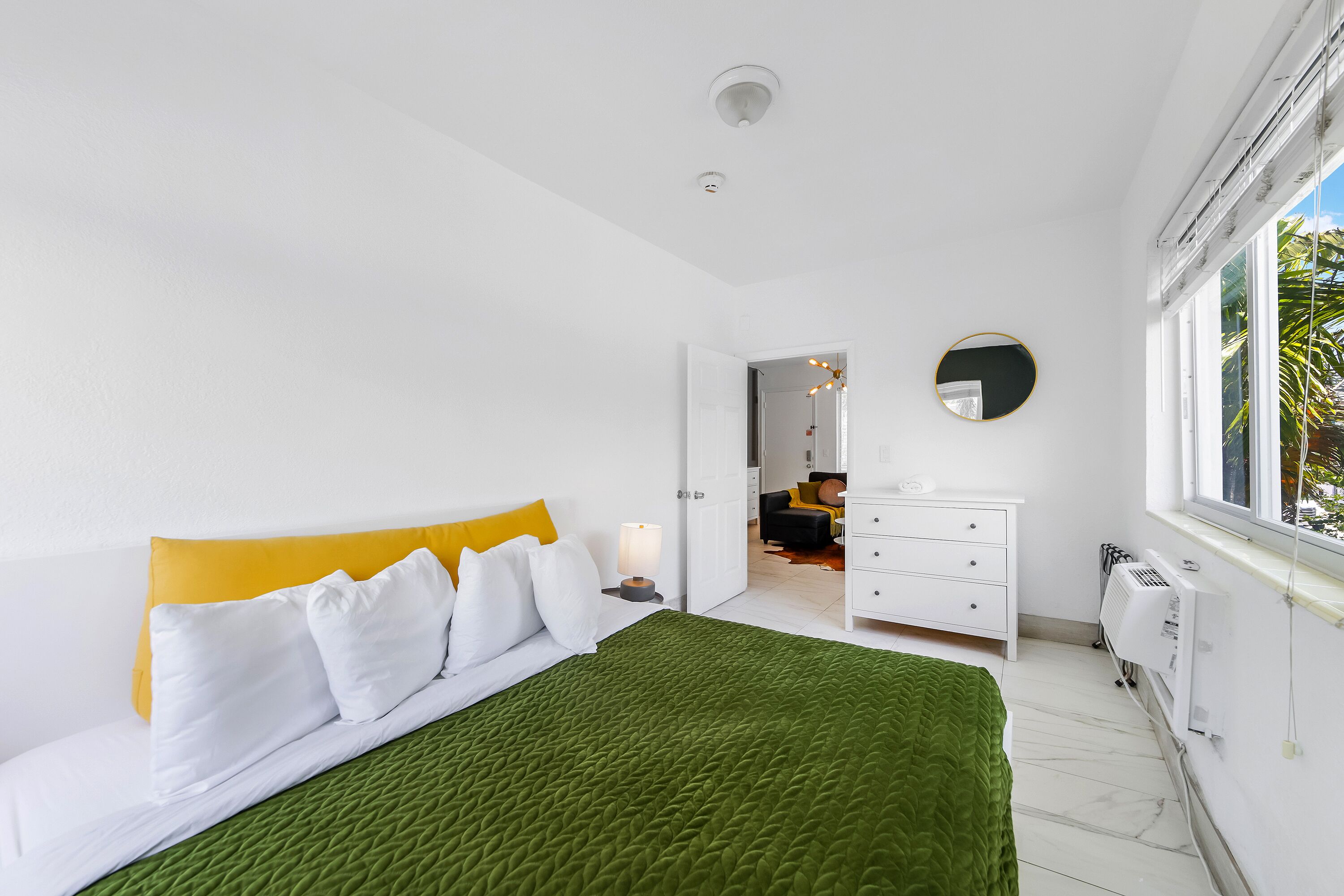 A bedroom with a bed, a dresser, a mirror, and a window.