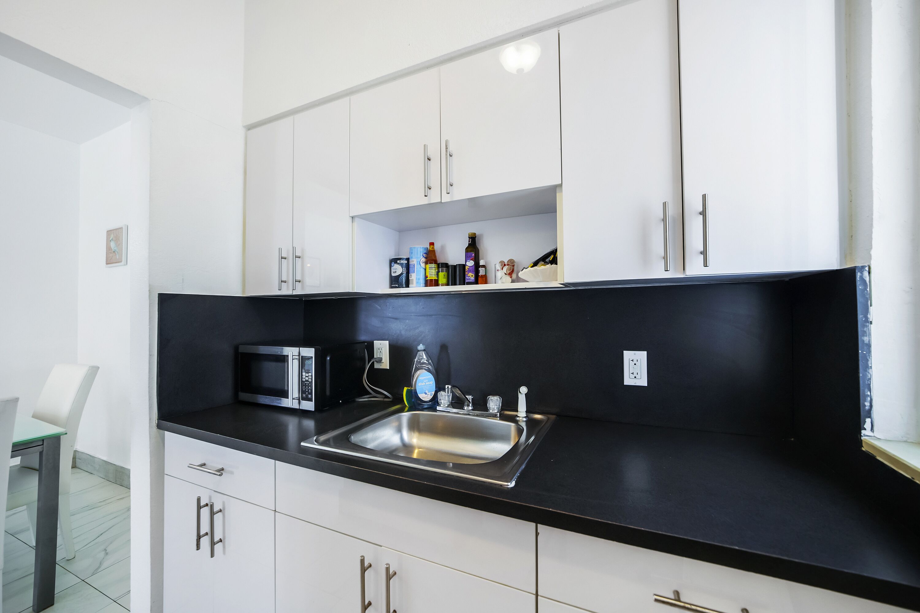 Een moderne keuken met witte kasten, een zwart aanrecht, een roestvrijstalen spoelbak en diverse keukenbenodigdheden.