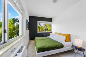 Ein modernes Schlafzimmer mit Bett, Nachttisch mit Lampe, Fenster mit Blick auf Grünflächen und Heizkörper.