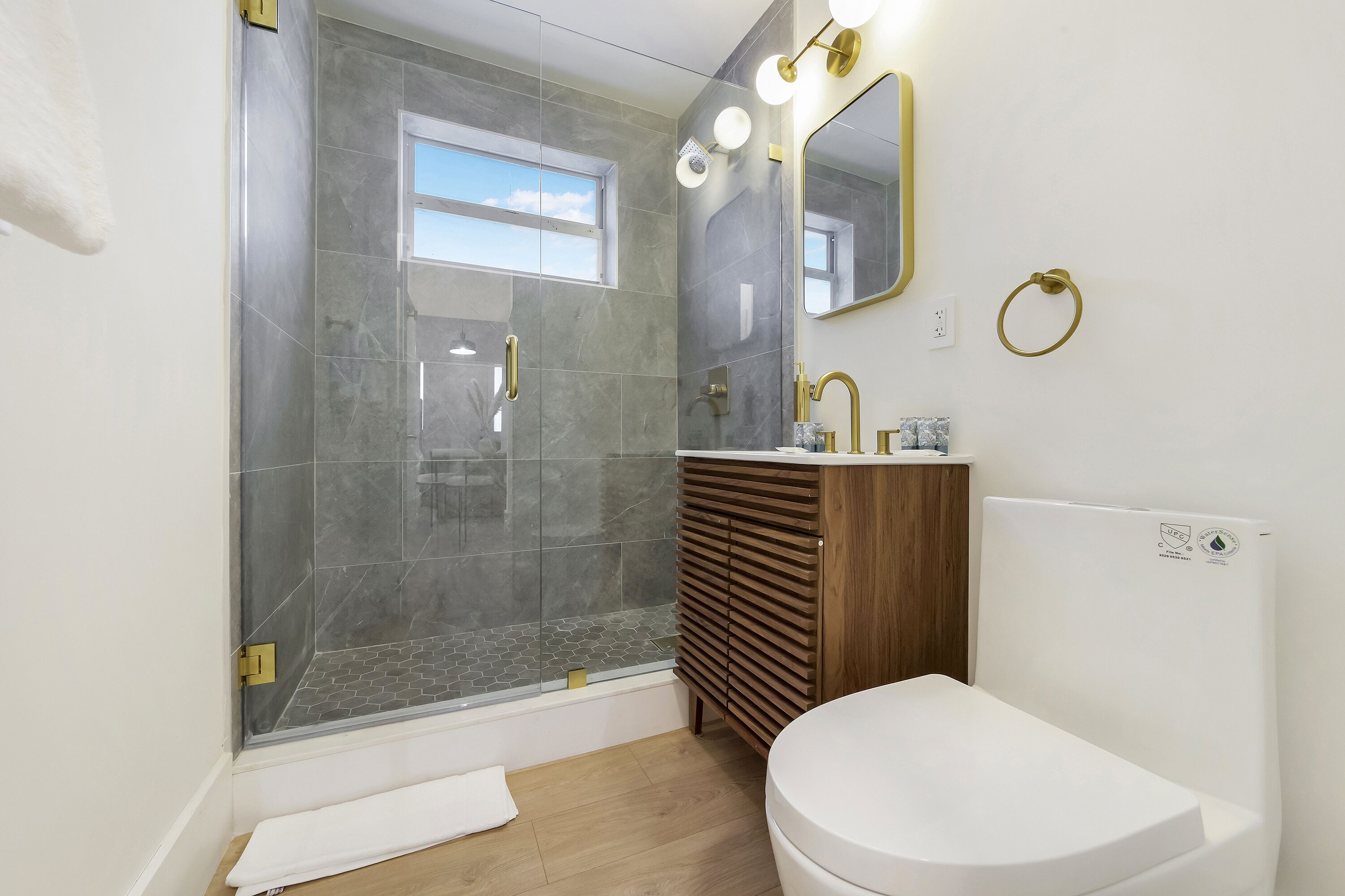 A modern bathroom with a shower, toilet, vanity, and a large mirror with lights.