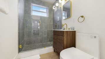 A modern bathroom with a shower, toilet, vanity, and a large mirror with lights.
