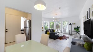 A modern kitchen with a refrigerator, dining table, and chairs. There is a living area with a sofa, coffee table, and a TV. - Harding 8040 Apts By At Mine Hospitality (Miami Beach)