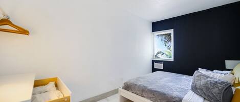 A bedroom with a bed, a wooden dresser, a window with a view, and a ceiling light.