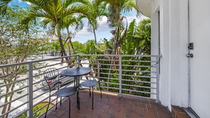 A balcony with a white railing, a table with chairs, and a view of palm trees and buildings. - Harding 8040 Apts By At Mine Hospitality (Miami Beach)