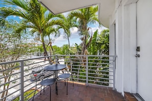 A balcony with a white railing, a table with chairs, and a view of palm trees and buildings. - Harding 8040 Apts By At Mine Hospitality (Miami Beach)